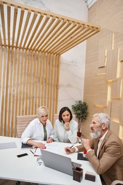 Orta yaşlı ve dövmeli emlakçı lezbiyen çiftle gayrimenkul alımını tartışıyor.