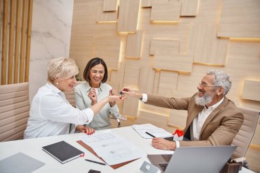Dövmeli emlakçı, yeni evden anahtarı orta yaşlı, neşeli lezbiyen çifte veriyor.
