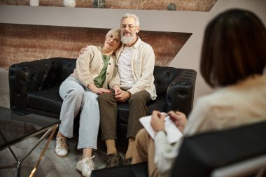 Mutlu orta yaşlı çift aile terapisi sırasında kucaklaşıp deri koltukta oturuyor.