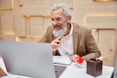 Dövmeli mutlu emlakçı ofiste dizüstü bilgisayarla online danışmanlık yapıyor.