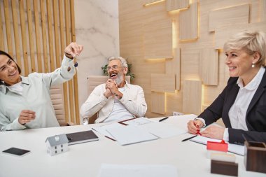 Yeni evin anahtarını elinde tutan mutlu bir kadın. Heyecanlı, orta yaşlı bir koca ve emlakçı.