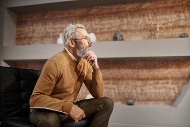 Gözlüklü orta yaşlı bir psikolog defter yanında kalem tutuyor ve oturum sırasında dinliyor.