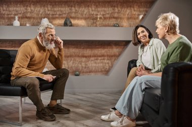 middle aged psychologist in glasses listening to happy lesbian couple during therapy session clipart