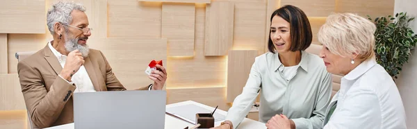 stock image middle aged realtor holding house model near interracial lgbt couple in real estate office, banner