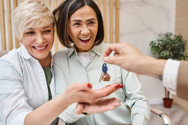 stock image middle aged realtor giving house key to excited interracial lgbt family in real estate office