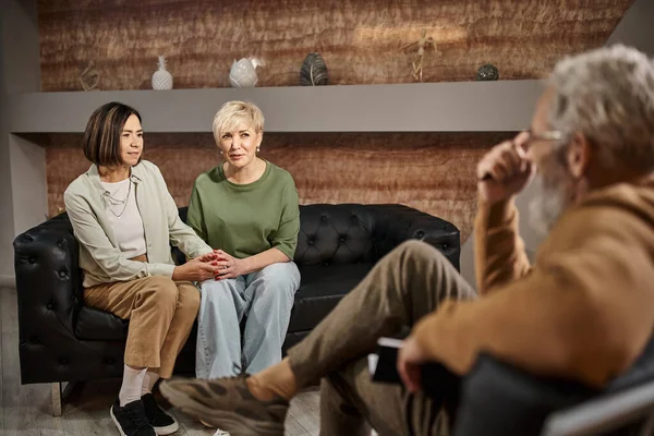 stock image middle aged lesbian couple talking and sitting on couch near psychologist during session