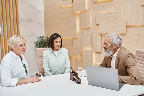 stock image smiling middle aged multicultural lgbt couple sitting next to bearded realtor in real estate office