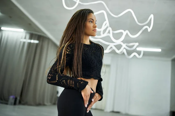 Stock image young long-haired african american woman in black attire rehearsing dance in studio, artistry