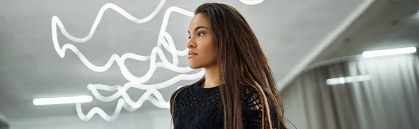 stock image expressive long-haired african american woman in black attire rehearsing dance in studio, banner