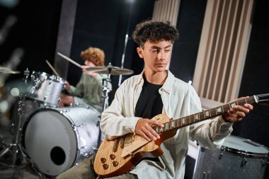 Bulanık bateristinin yanında gitar çalan sıradan giyinmiş sevimli genç bir çocuk.