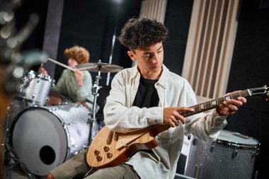 good looking talented teenage boy playing guitar next to his blurred drummer, musical group clipart