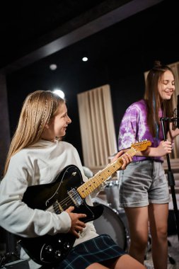 Gitar çalan neşeli sarışın genç kıza odaklan ve esmer arkadaşına şarkı söylerken bak.