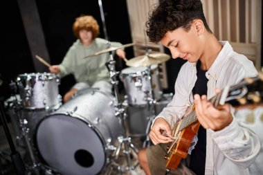 Stüdyoda bulanık bateristinin yanında gitar çalan yetenekli, tapılası genç çocuğa odaklan.