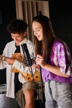 Arkadaşının gitar çalarken mikrofona şarkı söyleyen mutlu genç kızın dikey görüntüsü.