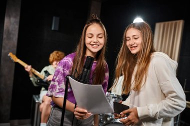Arkaplanda bulanık gitarist çocukla şarkı söyleyen ve şarkı sözlerine bakan neşeli genç kızlara odaklan.
