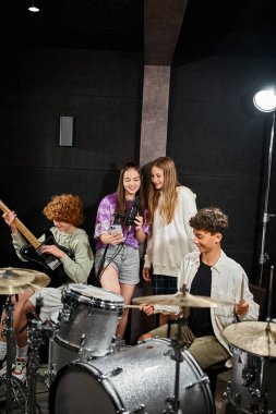 Neşeli genç kızlar şarkı söylerken, erkekler bateri ve gitarlarını stüdyoda, müzik grubunda çalıyorlar.