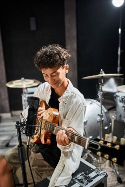 Neşeli, sevimli, yetenekli, günlük kıyafetleriyle gitar çalan ve mutlu bir şekilde gülümseyen genç çocuk.
