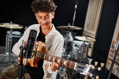Sevimli, yetenekli, sıradan kıyafetler içinde gitarını çalıp stüdyoda mutlu bir şekilde gülümseyen genç kız.