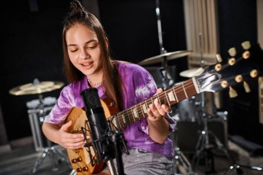 Neşeli, sevimli, genç gitarist, rahat kıyafetiyle gitar çalıyor ve şarkı söylüyor.