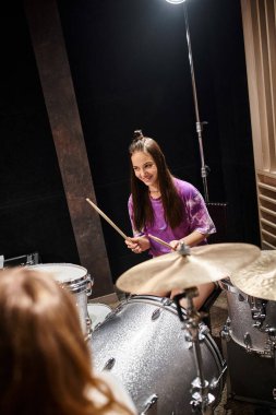 cheerful pretty teenage girl in vibrant clothes playing guitar and smiling happily in studio clipart