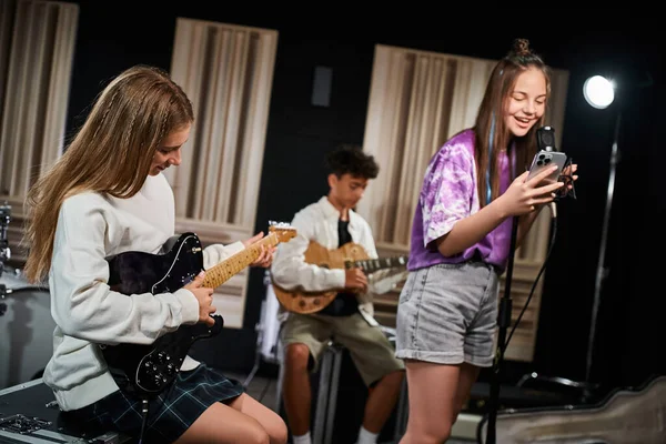 stock image jolly cute teenage girl in everyday attire singing happily next to her friend on guitars in studio