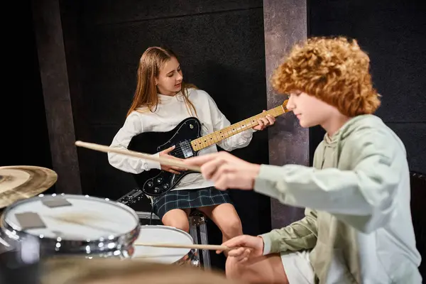 stock image focus on concentrated pretty teenage girl playing guitar next to her blurred adorable drummer