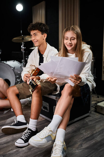 jolly teenage girl looking at lyrics next to her friend with braces playing guitar, musical group