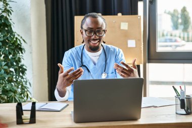 young joyous african american doctor with glasses consulting someone by phone and gesturing actively clipart