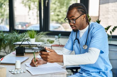 concentrated african american doctor with glasses taking notes and consulting by phone, telehealth clipart