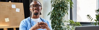 Steteskoplu, gözlüklü, gülümseyen ve kameraya bakan neşeli Afrikalı Amerikalı doktor.