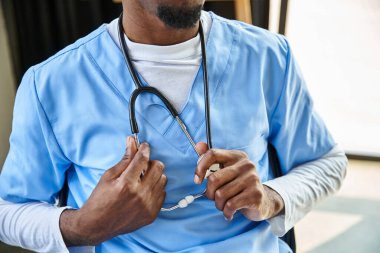 Ofisindeyken boynunda steteskop olan Afrikalı Amerikalı genç bir doktor.