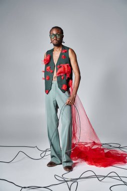 Güzel görünümlü, şık güneş gözlüklü Afro-Amerikan adam hareket halinde duruyor ve kameraya bakıyor.