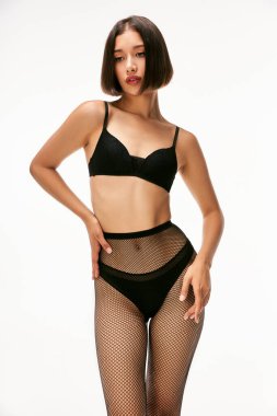 Siyah iç çamaşırlı ve file çoraplı güzel bir Asyalı manken. Beyaz kalçayla poz veriyor.