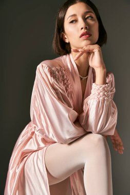 Rüya gibi ve pembe ipek bornoz ve gri arka planda beyaz külotlu çorap giyen Asyalı genç bir kadın.