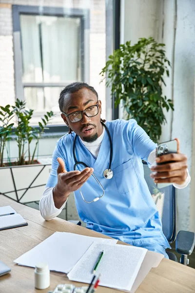 focused african american doctor with stethoscope consulting patient by mobile phone, telehealth