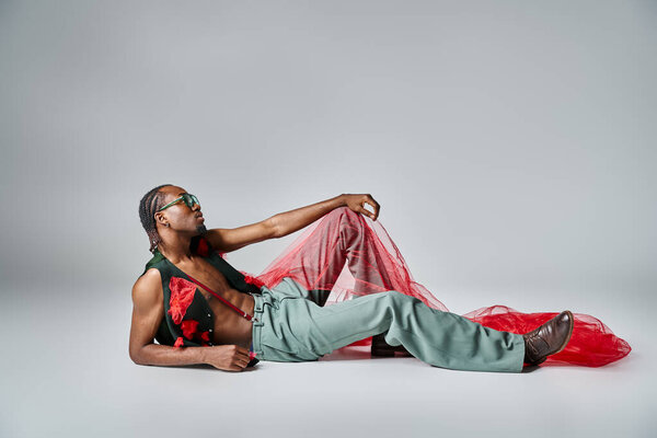 Alluring african american man in fashionable attire with red tulle fabric reclining on floor