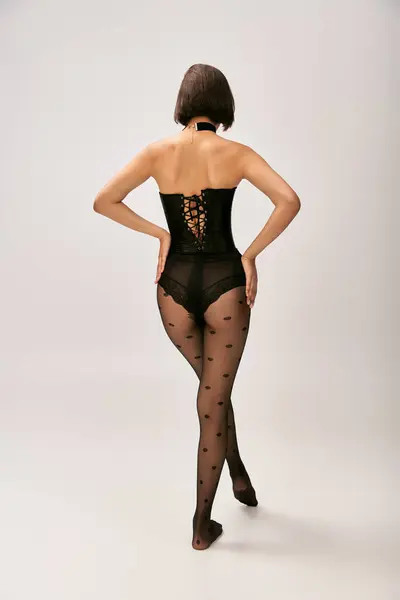 back view of woman in corset and polka dot tights posing on white background, female buttocks