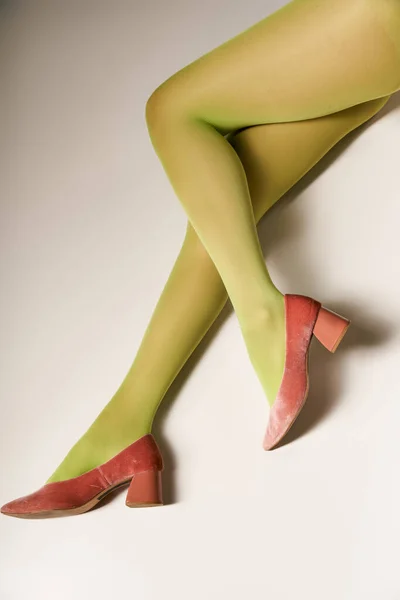 cropped view of young woman in green nylon tights lying on grey background, hosiery concept