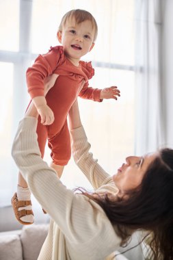 Güzel, neşeli ev elbiseli bir kadın. Küçük kızıyla aktif olarak oynuyor. Aile kavramı.