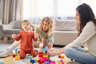 Neşeli lezbiyen çift evde oyuncak bebekleriyle oynuyorlar, aile kavramı.