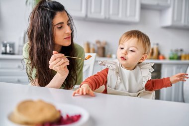 Çekici esmer kadın kahvaltı sırasında küçük bebeğini besliyor, aile kavramı.