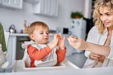Ev elbiseli çekici sarışın kadın kahvaltı sırasında bebeğini besliyor, aile kavramı.