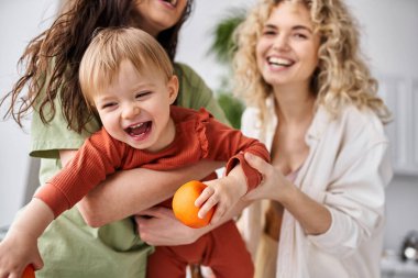 cheerful lesbian couple having fun together with their cute baby girl holding tangerines, family clipart