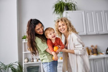 merry lesbian couple having fun together with their cute baby girl holding tangerines, family clipart