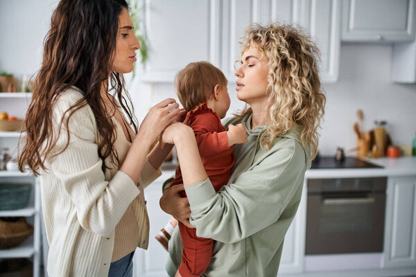 beautiful lgbt couple holding their adorable baby girl in hands and comforting her, family concept