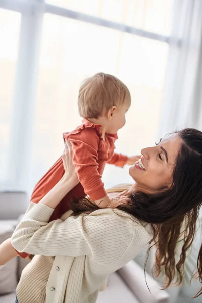 stock image beautiful happy woman in cozy homewear playing actively with her baby daughter, family concept