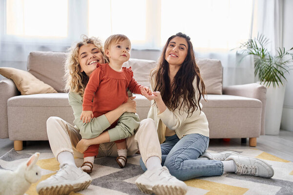 attractive joyful lgbt couple having great time together with their daughter at home, family concept