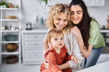 Ev elbiseli neşeli bir çift ellerinde kaşıklarla kızlarıyla mutfakta vakit geçiriyorlar.