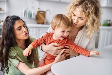 Ev elbiseli çekici lezbiyen çift ağlayan kızlarını mutfakta rahatlatıyorlar, aile kavramı.