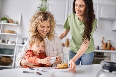 happy charming lgbt couple in homewear having great time with their daughter at breakfast, family clipart